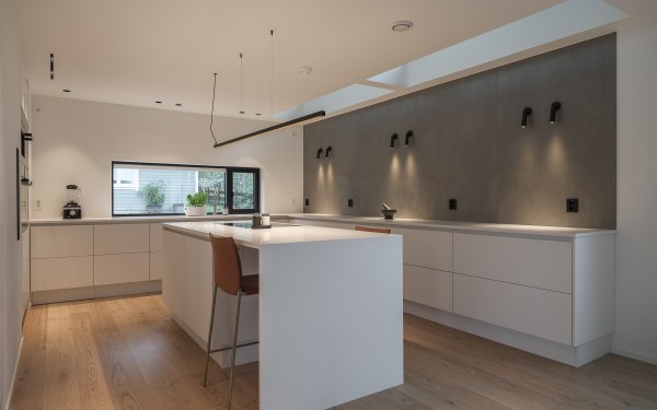 Stort moderne kjøkken med hvit innredning, tregulv, grå bakvegg og sorte lamper. Foto: Håvard Løberg for Stokkan Lys AS.